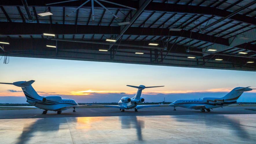 tail view of three business jets looking out of hangar at sunset