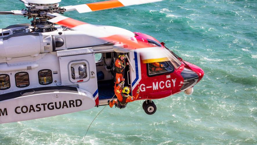 Irish Coast Guard helicopter in flight over ocean with service members repelling into water