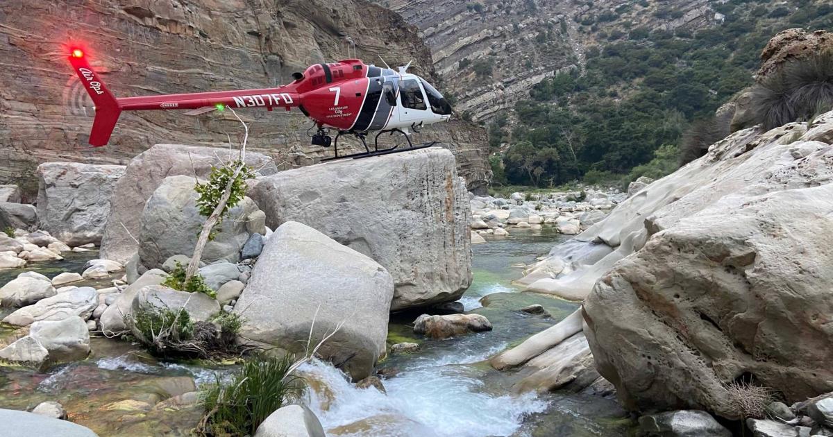 Los Angeles Fire Department Bell 505 atop large boulder in creek surrounded by mountains